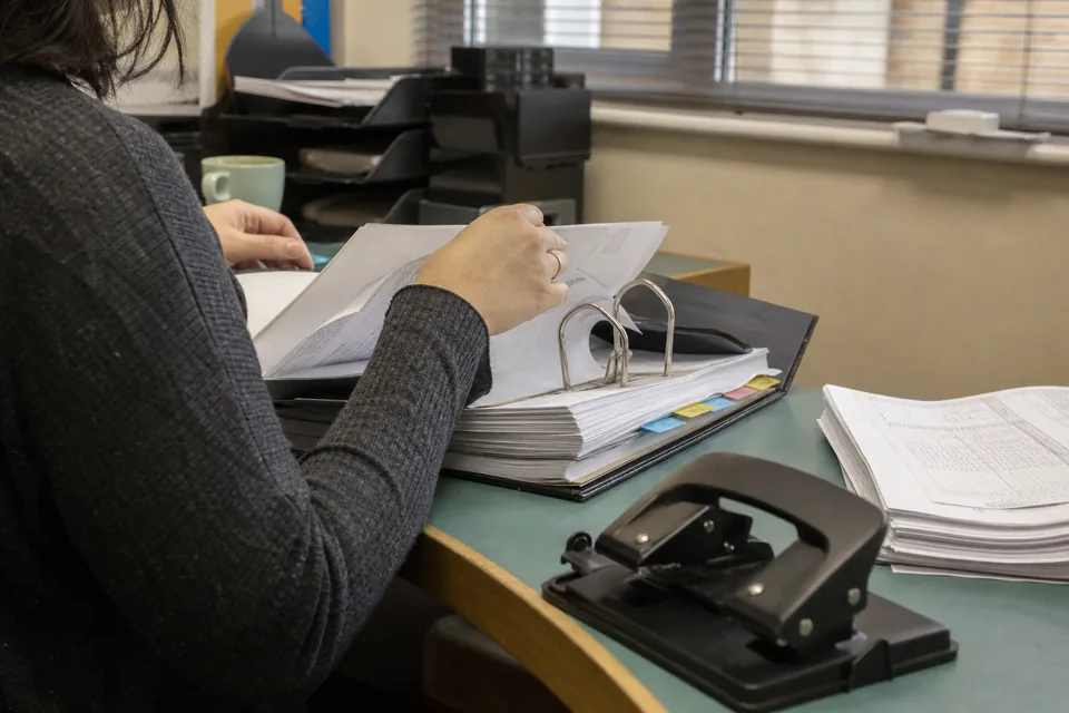 Hands filing printed statement pages into a client binder behind tabbed dividers on an accounting office desk