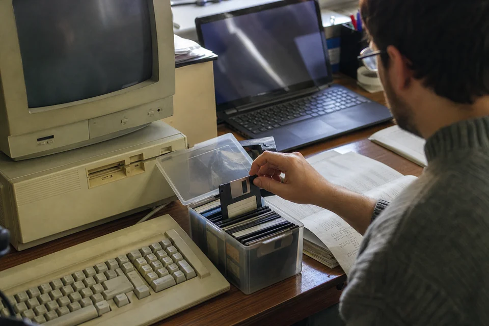 Old desktop computer with a floppy disk box and printed transaction listings on a home office shelf