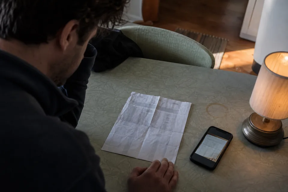 A phone lying on a desk showing a photo of a paper statement, next to the creased original page