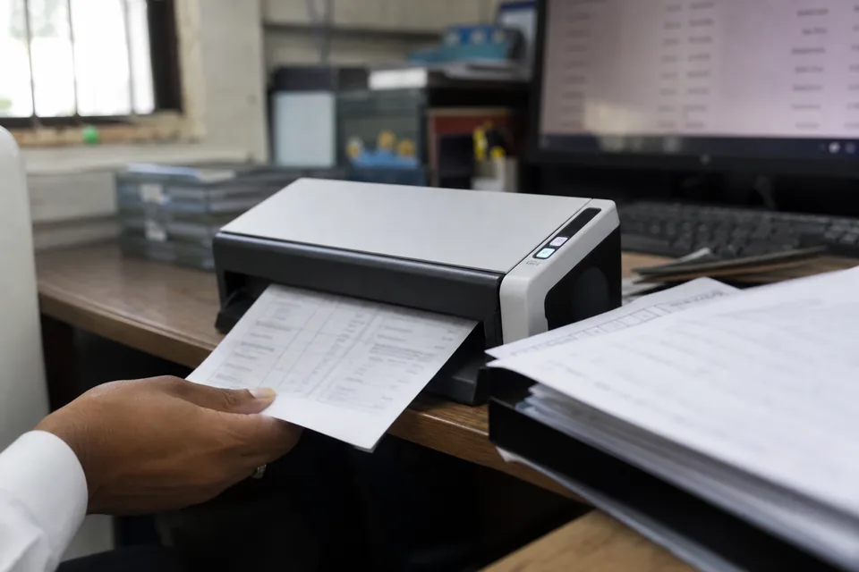 A paper bank statement being fed into a desktop scanner in a small accounting office